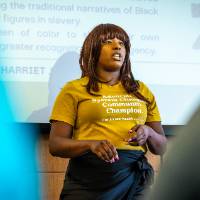 close-up of a woman in a yellow shirt presenting in front of a projector